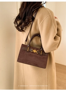 Detalle de bolso vintage de ante marrón oscuro con hebilla de corazón dorado sobre abrigo