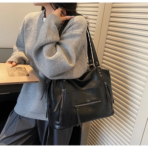 Detail of a black leather tote bag showing soft texture and decorative side zippers
