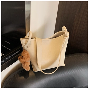 Close-up of beige lychee grain faux leather shoulder bag with a brown teddy bear pendant