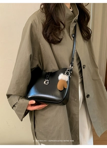 Detail of a black leather shoulder bag with a silver G buckle and a glove-shaped charm