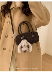 Brown retro suede Boston bag with plush rabbit charm worn on a camel wool coat