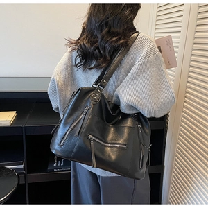 Detail of black PU leather motorcycle tote bag with silver zippers and long pullers