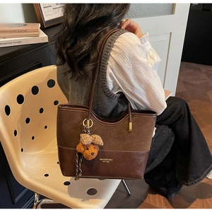 Detail of brown suede tote bag featuring a cute teddy bear charm and brand logo