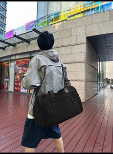 Close-up of black waterproof nylon travel bag worn by a model in a modern urban street setting