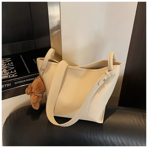 Detail of cream lychee leather bucket bag with a cute brown plush bear charm accessory