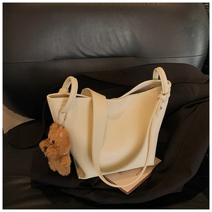 Detail of cream white pebbled leather bucket bag featuring a brown teddy bear pendant