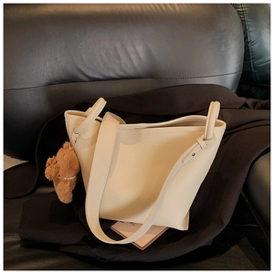 Detail of creamy white pebble grain leather bucket bag with a brown plush bear charm