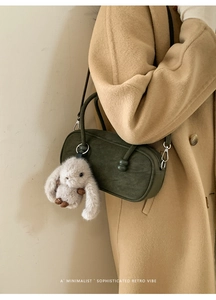 Dark green matte Boston bag with plush bunny charm worn over a camel wool coat