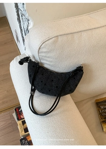 Dettaglio borsa a mezzaluna in maglia a pois su un divano con libri decorativi