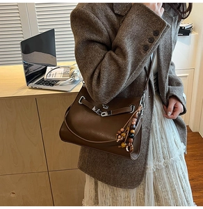 Detail of brown vintage leather tote featuring metal buckle and boho beaded tassel