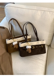 Detail of suede shoulder bags with faux fur trim and heart-shaped pompom charm on a sofa