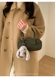Detail of dark green matte Boston bag with a cute plush rabbit charm on a wool coat