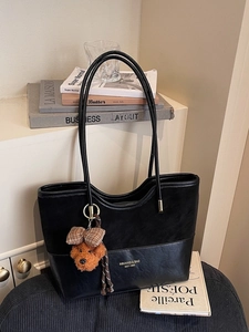Black stylish tote bag with plush teddy bear pendant on a minimalist home background