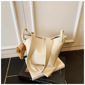 Detail showing creamy white pebbled leather tote with a cute brown plush bear charm