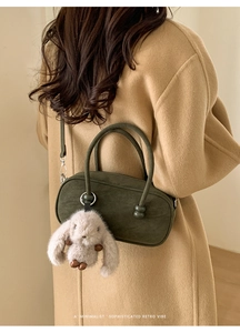 Retro dark green Boston shoulder bag with plush bunny charm styled on a beige coat