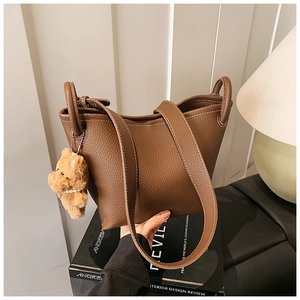 Detailed view of brown lychee grain leather bucket bag with plush bear charm and white stitching
