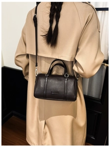 Detail view of a dark brown lychee leather Boston bag worn with a classic khaki trench coat