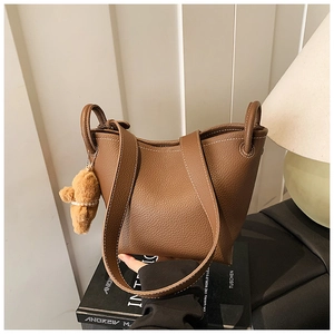 Detail of brown lychee grain leather bucket bag with contrast stitching and bear charm