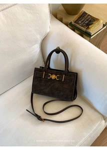 Detalle de bolso de ante marrón oscuro en sofá blanco con herrajes dorados