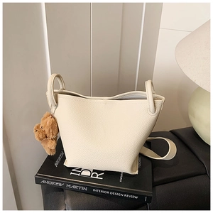 Detail of cream bucket bag with lychee texture and a brown plush bear charm