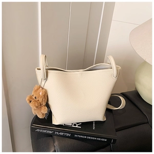 Detail view of beige lychee leather bucket bag with cute brown bear plush charm and handles