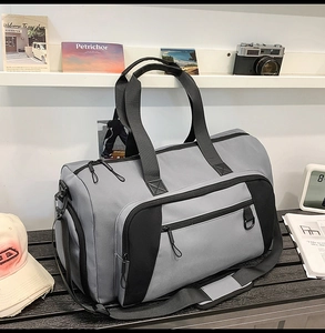 Detail of grey duffle bag with black straps and side compartment on a wooden bench