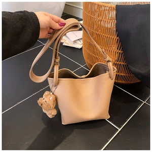 Detail of khaki bucket bag in litchi grain leather with brown plush bear charm