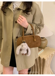 Detailed view of a brown suede Boston bag with a cute white rabbit plush charm