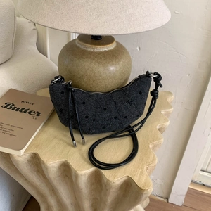 Vue détaillée du sac croissant gris foncé à pois avec bandoulière tressée sur table en bois
