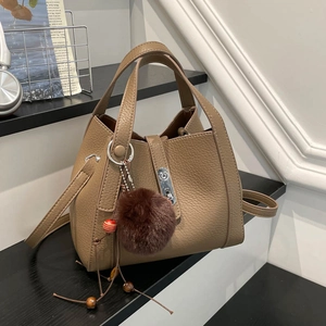 Gros plan du sac seau en cuir marron avec fermoir argenté et pompon en peluche