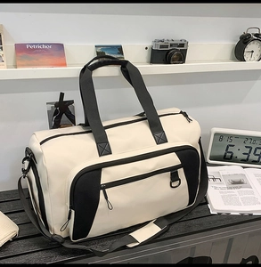 Detail view of large cream travel bag with black handles and side straps on a desk