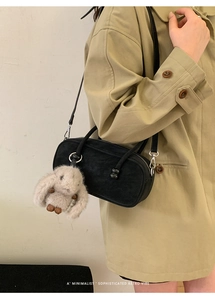 Detail of black oval suede crossbody bag with cute plush rabbit charm on side