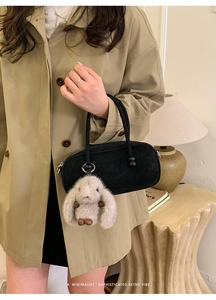 Detail of retro black minimalist handbag with plush rabbit charm on vintage coat