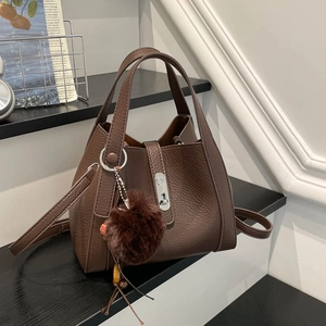 Détail du sac seau en cuir marron à motif litchi avec fermoir argenté et pompon en fourrure