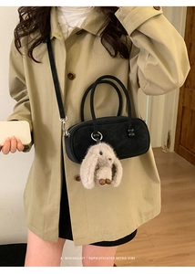 Close-up of minimalist black handbag with plush bunny charm and beaded detail on coat