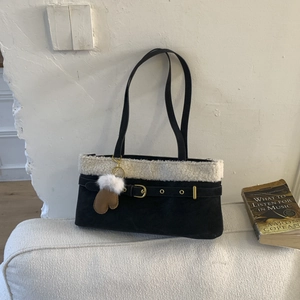 Detail of black suede shoulder bag with faux fur trim, gold buckle, and glove charm