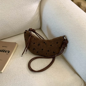 Détail d'un sac croissant marron foncé avec pois et nœuds sur un canapé douillet
