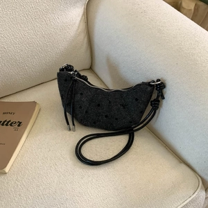 Détail du sac croissant noir à pois avec bandoulière nouée sur un canapé blanc