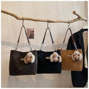 Three suede tote bags in grey, black and brown hanging on rustic wooden branches