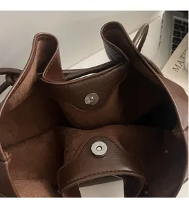 Close-up of shiny silver magnetic buckle on deep brown leather bucket tote bag