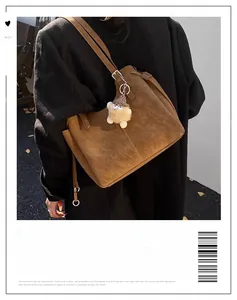 Brown suede tote bag with plush monster charm worn by a model in a street style view