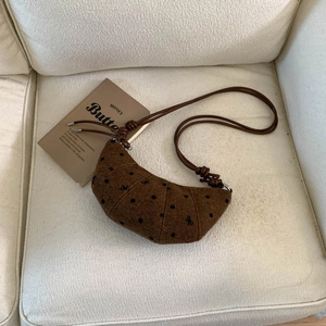 Détail d'un sac croissant marron en tweed à pois sur fond de textile blanc doux
