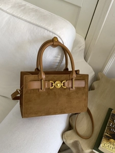 Bolso bandolera de ante marrón con hebilla de corazón dorado en un sofá blanco