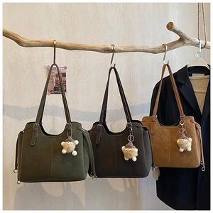 Close-up of three large suede tote bags in green, brown, and camel with plush monster charms