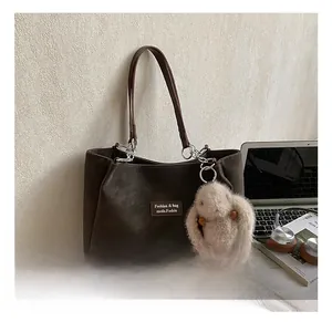 Detail of coffee brown matte tote bag with plush bunny charm and laptop on white surface