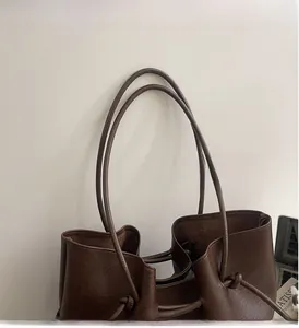 Detail view of dark brown tote bag showing knotted cylindrical handles and leather texture