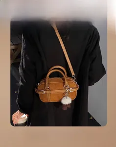 Detail of a brown suede Boston bag featuring leather trim and a white fluffy charm