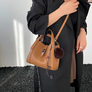 Détail du sac seau en cuir marron avec poignée, fermoir métal et breloque pompon