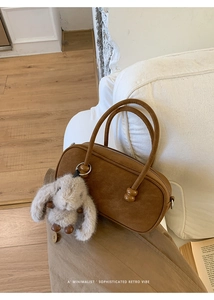 Close-up of brown suede pillow bag featuring wooden bead accents and a plush bunny charm