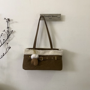 Detail of dark brown suede shoulder bag with plush white faux fur trim and glove pendant